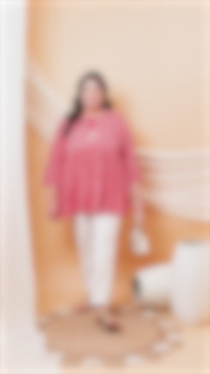 Plus size woman wearing a Curvisha pink and white Bandhani print cotton tunic with 3/4 sleeves and white trousers.